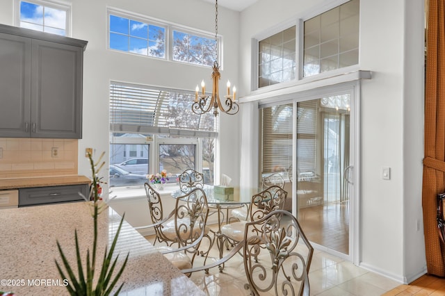 dining space featuring baseboards, a high ceiling, light tile patterned floors, and a notable chandelier