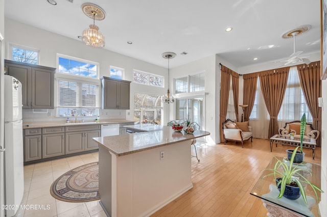 kitchen featuring gray cabinetry, white appliances, a kitchen island, a sink, and an inviting chandelier