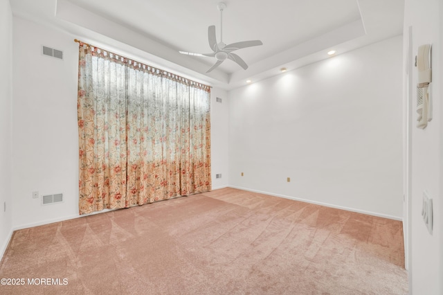 carpeted empty room with a ceiling fan, a raised ceiling, visible vents, and baseboards