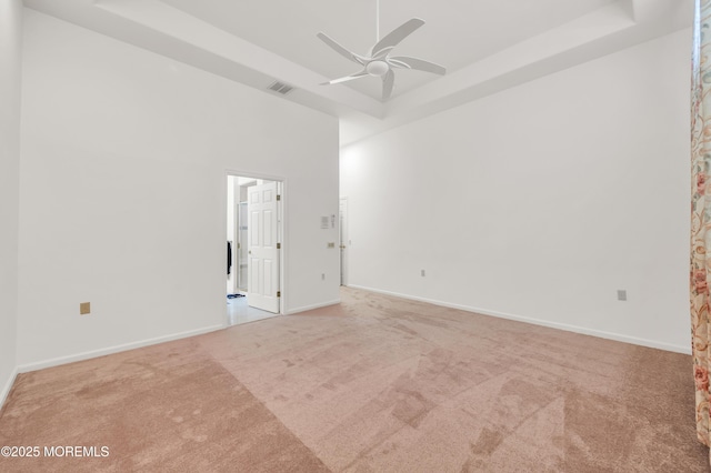 carpeted spare room with baseboards, a high ceiling, a tray ceiling, and a ceiling fan