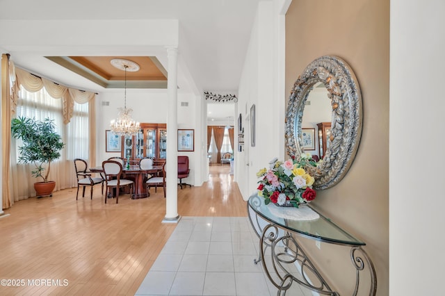 entryway featuring light wood-type flooring, ornate columns, a tray ceiling, and a notable chandelier