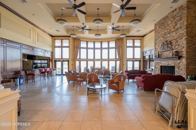 living room with ornamental molding, a stone fireplace, light tile patterned flooring, and a towering ceiling