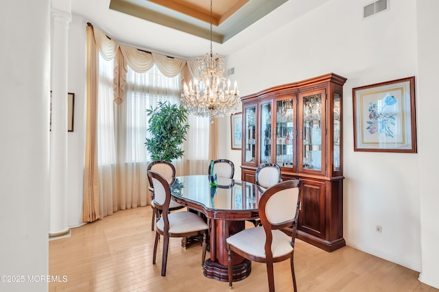 dining area featuring a notable chandelier, visible vents, baseboards, light wood-type flooring, and a tray ceiling