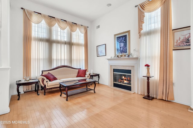 living area with a premium fireplace, visible vents, and wood finished floors