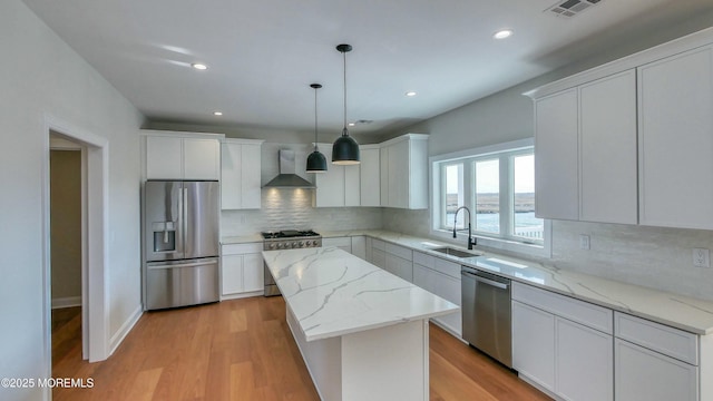 kitchen featuring stainless steel appliances, a sink, a kitchen island, visible vents, and wall chimney range hood