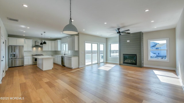 kitchen with open floor plan, stainless steel appliances, wall chimney exhaust hood, and visible vents