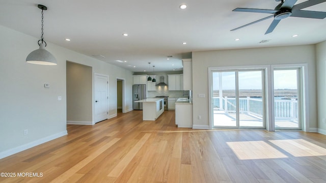 kitchen featuring white cabinets, open floor plan, light countertops, wall chimney range hood, and appliances with stainless steel finishes