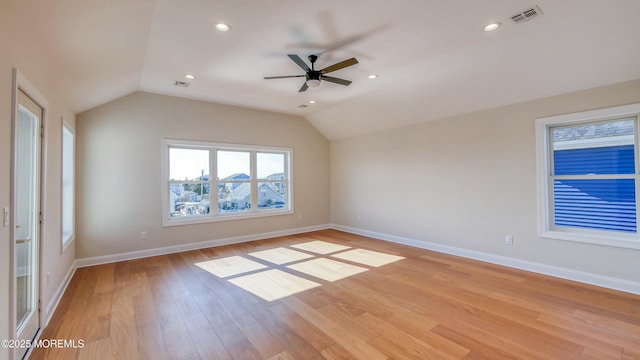 empty room with vaulted ceiling, light wood-type flooring, visible vents, and baseboards