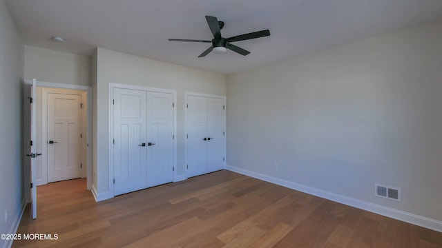 unfurnished bedroom with multiple closets, visible vents, ceiling fan, wood finished floors, and baseboards