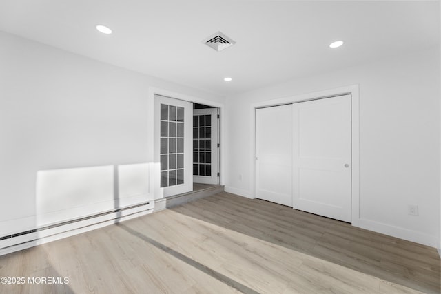 interior space with a baseboard heating unit, recessed lighting, wood finished floors, and visible vents