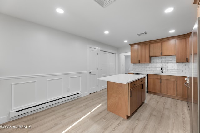 kitchen featuring visible vents, a sink, a baseboard heating unit, a kitchen island, and light wood finished floors