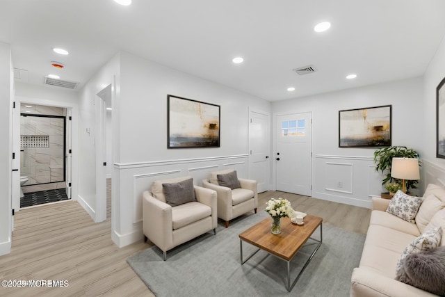 living area featuring light wood finished floors, visible vents, recessed lighting, and a decorative wall