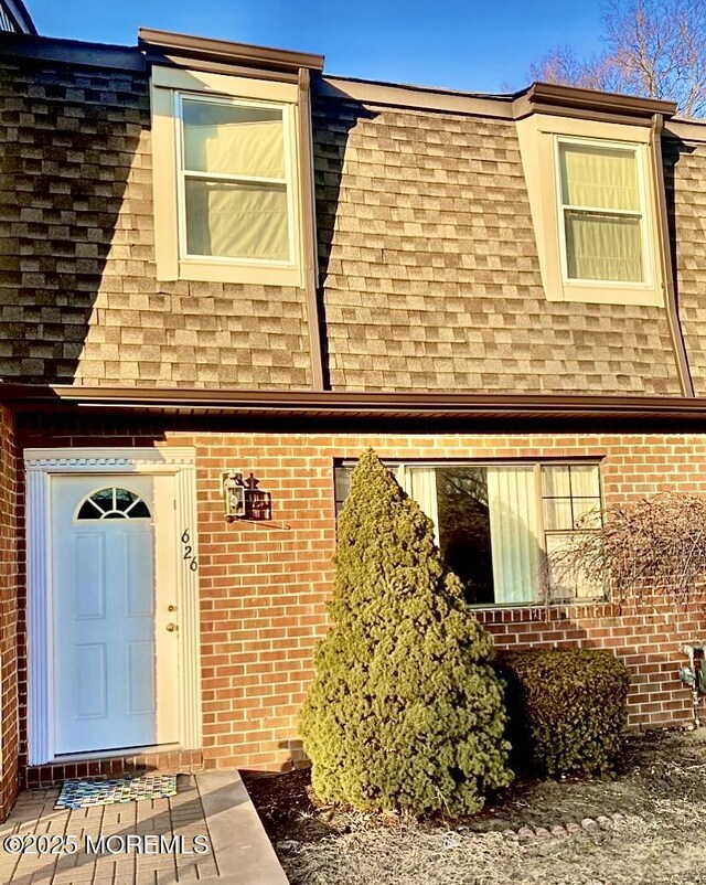 exterior space featuring a shingled roof, mansard roof, and brick siding