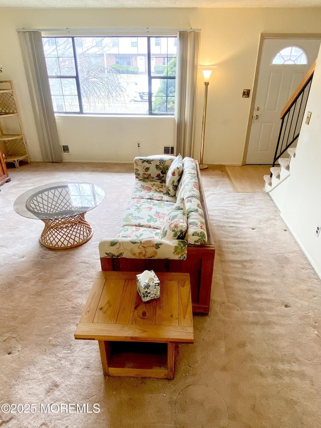 carpeted living area with stairs, a healthy amount of sunlight, and visible vents
