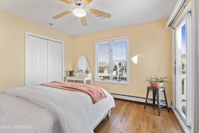 bedroom with a baseboard radiator, a closet, visible vents, a ceiling fan, and wood finished floors