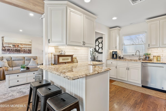 kitchen with light stone counters, a breakfast bar area, a sink, light wood-style floors, and stainless steel dishwasher