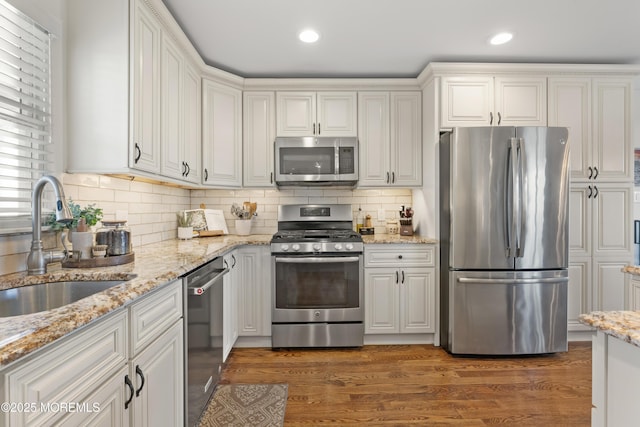 kitchen with tasteful backsplash, appliances with stainless steel finishes, white cabinetry, a sink, and wood finished floors