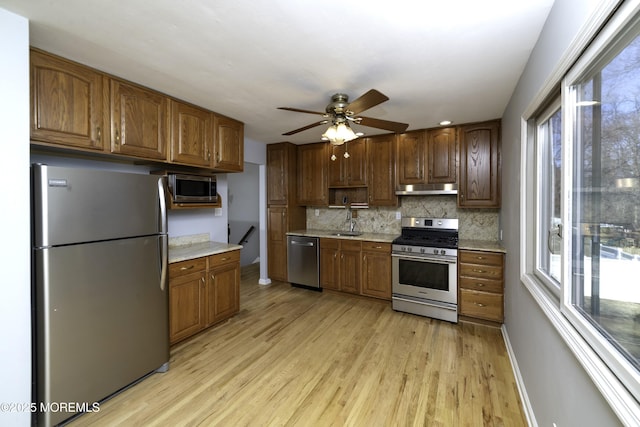 kitchen featuring tasteful backsplash, baseboards, appliances with stainless steel finishes, light wood-type flooring, and under cabinet range hood