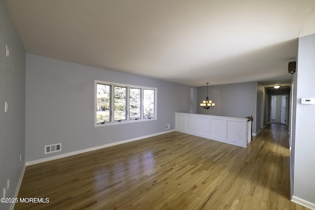 unfurnished living room featuring baseboards, visible vents, a chandelier, and wood finished floors