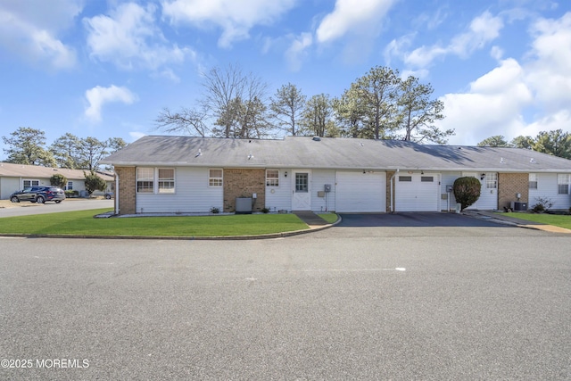 view of front of home featuring aphalt driveway, brick siding, an attached garage, cooling unit, and a front lawn