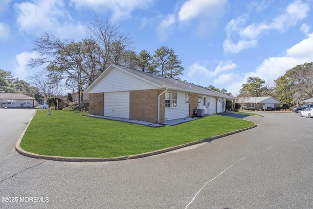 view of side of property featuring a garage, driveway, central AC unit, a lawn, and brick siding