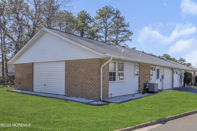 single story home featuring aphalt driveway, an attached garage, central AC, brick siding, and a front lawn