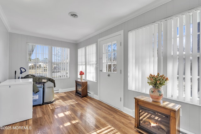 interior space with a baseboard heating unit, visible vents, ornamental molding, and wood finished floors