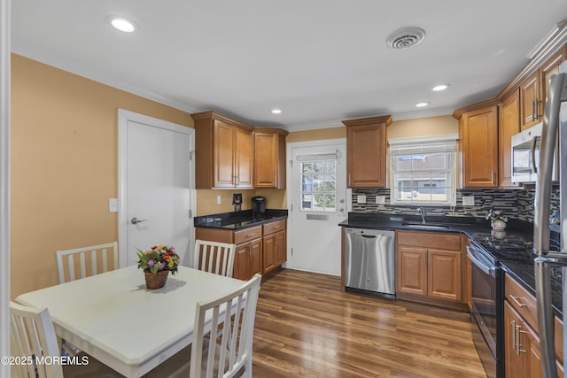 kitchen featuring stainless steel appliances, dark wood-style flooring, a sink, visible vents, and dark countertops