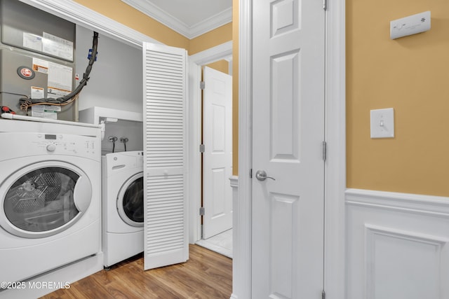 clothes washing area with laundry area, ornamental molding, washer and clothes dryer, and wood finished floors