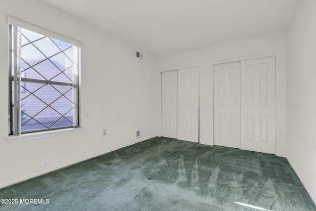 unfurnished bedroom with visible vents, multiple windows, two closets, and carpet floors