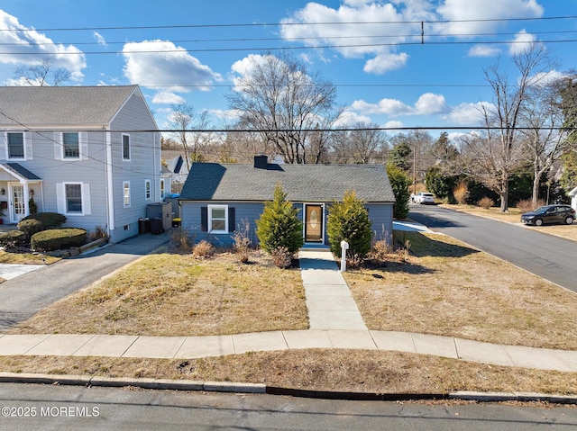 view of front of house with aphalt driveway, roof with shingles, and a chimney