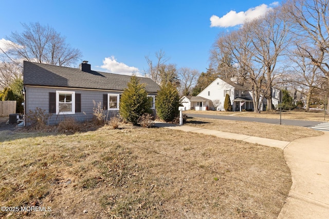 view of front of home featuring roof with shingles, a chimney, central AC unit, and a front yard