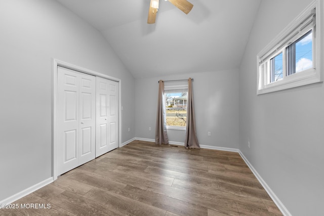 unfurnished bedroom featuring lofted ceiling, a closet, baseboards, and wood finished floors