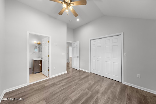 unfurnished bedroom with lofted ceiling, a closet, ensuite bath, wood finished floors, and baseboards