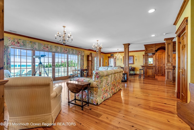 living room with decorative columns, visible vents, light wood-style flooring, an inviting chandelier, and ornamental molding