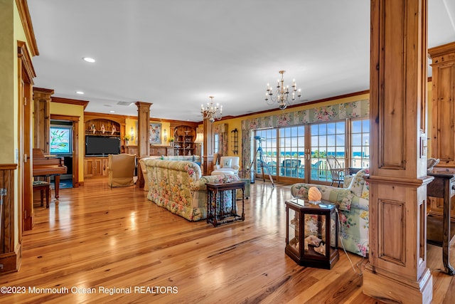 living room featuring crown molding, light wood-type flooring, ornate columns, a chandelier, and recessed lighting