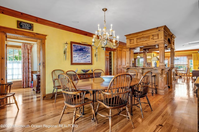 dining area with ornamental molding, a chandelier, light wood-style flooring, and ornate columns