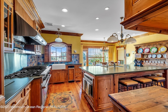 kitchen with a breakfast bar, stainless steel range, brown cabinetry, a sink, and extractor fan