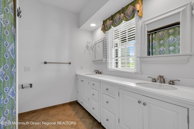 full bathroom featuring double vanity, curtained shower, a sink, and baseboards