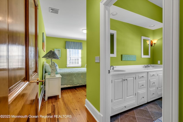 bathroom with double vanity, wood finished floors, a sink, and visible vents