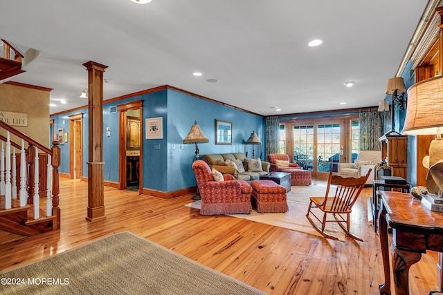 living area featuring baseboards, light wood-style floors, ornamental molding, stairway, and ornate columns