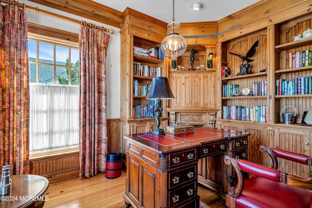 office space featuring wooden walls, wainscoting, light wood-style flooring, built in shelves, and a notable chandelier