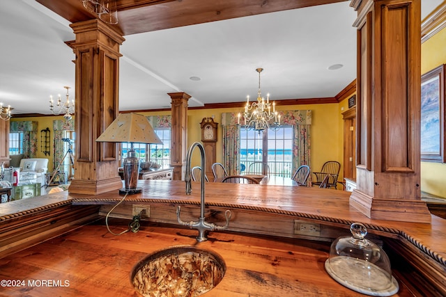 kitchen featuring decorative columns, a chandelier, brown cabinetry, and crown molding