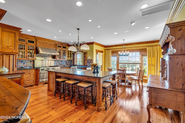 kitchen featuring visible vents, brown cabinetry, dark countertops, wall chimney exhaust hood, and high end stainless steel range