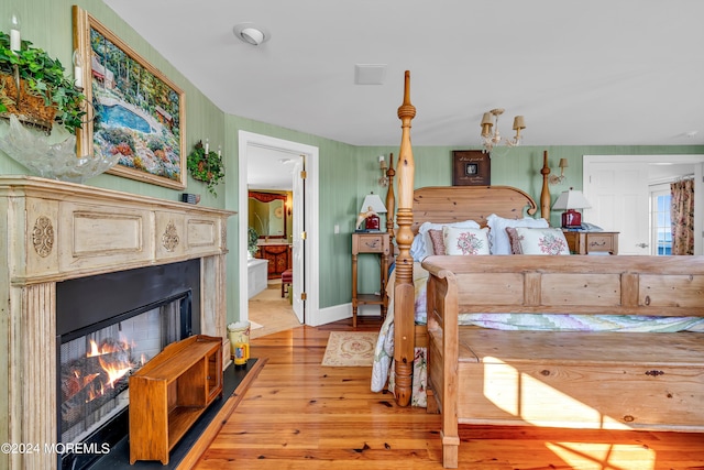 bedroom featuring a lit fireplace, light wood-type flooring, connected bathroom, and baseboards