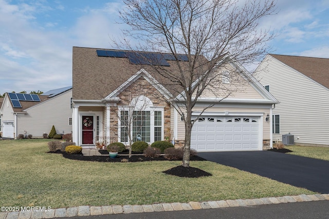 view of front facade with an attached garage, solar panels, stone siding, driveway, and a front yard