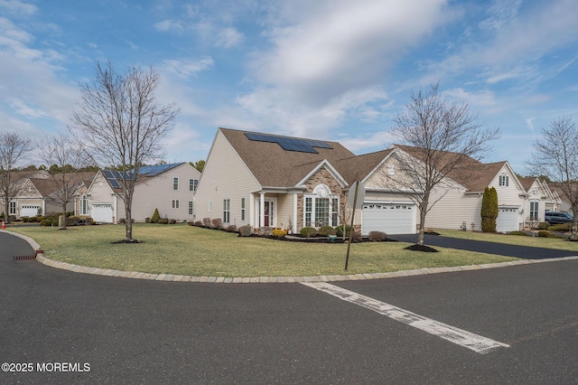 view of front of property featuring a residential view, roof mounted solar panels, an attached garage, and a front lawn