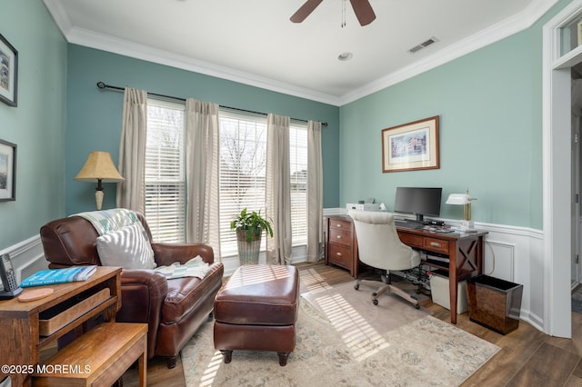 office featuring a wainscoted wall, visible vents, ornamental molding, ceiling fan, and wood finished floors