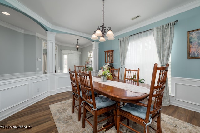 dining space featuring dark wood-style flooring, crown molding, visible vents, wainscoting, and ornate columns