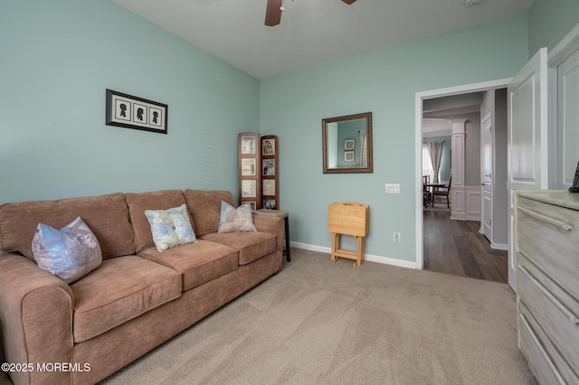 living area featuring carpet, baseboards, ceiling fan, and ornate columns